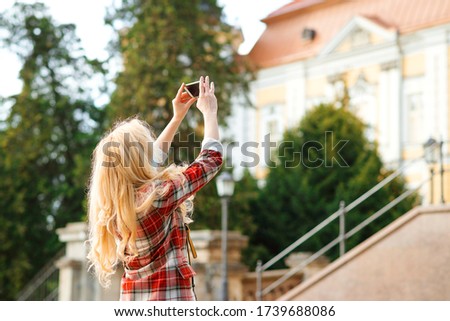 Stylish hipster girl using smartphone camera taking picture of architecture during sightseeing tour. Travel blogger shooting video for vlog in european city. Summer vacation.