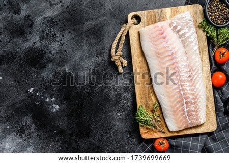 Raw cod fillet with and herbs on rustic wooden cutting board. Black background. Top view. Copy space