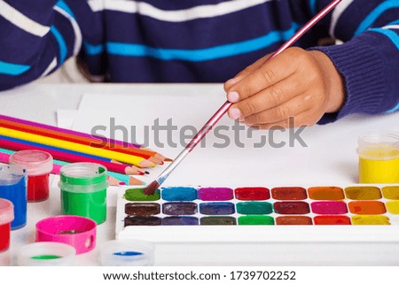 The child draws paints on white paper. The concept of the joy of art and learning