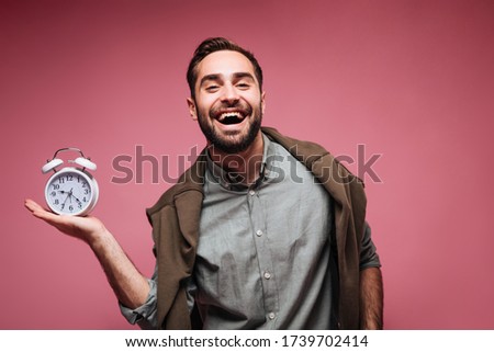 Handsome man in good humor posing with alarm clock on pink background