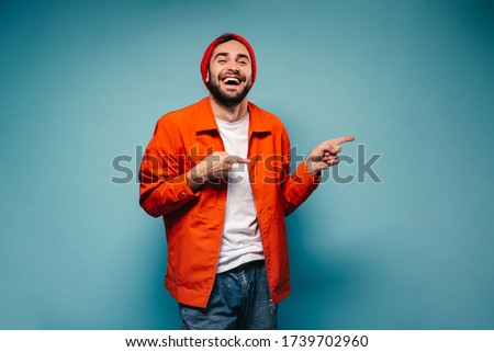 Man in orange jacket and hat has fun and points fingers to right