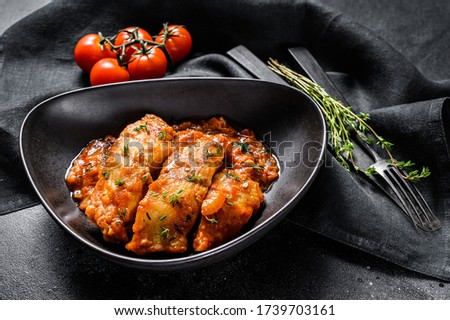 Baked Tilapia fish in tomatoes on a plate. Black background. Top view