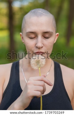 bald girl with a dandelion in her hand against the background of nature
