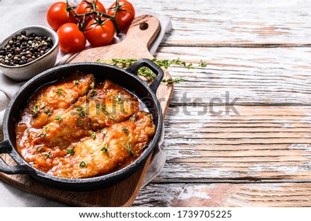 Baked halibut fish in a pan with tomato sauce. White wooden background. Top view. Copy space.