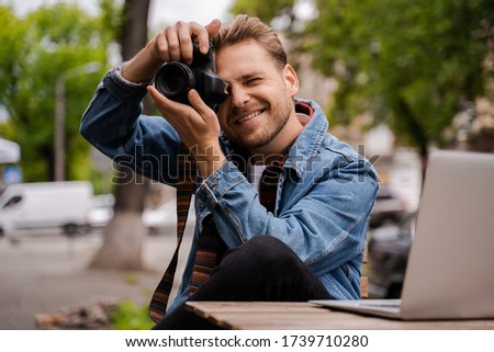 Photographer hipster traveller shooting outdoor in central city park, smiling and feel happy, freelancer work online and have a shoot for photo stock. Use laptop computer for key-wording