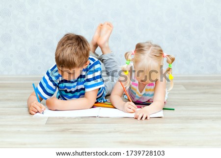 happy brother and sister draw while lying on the living room floor. Children draw with pencils at home.