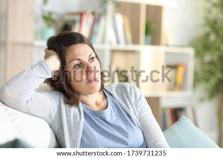Pensive adult woman thinking looking away sitting on the couch at home Royalty-Free Stock Photo #1739731235