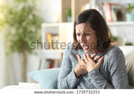 Middle age woman wheezing touching chest sitting on a couch at home Royalty-Free Stock Photo #1739732255