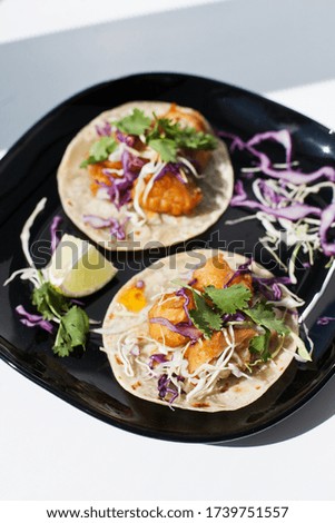 tacos with fried fishand vegetables on a black plate