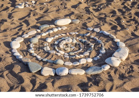 A spiral of stones is laid out on the sand. Pictures of stones. Beach ornament. Natural background of stones. Entertainment on the beach. Beach holiday. Infinity.