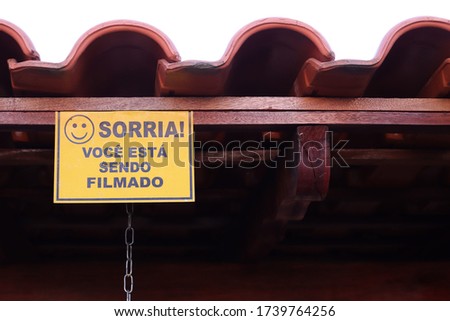 Photograph of a warning sign attached to the end of a roof, with the message "Smile, you are being filmed."