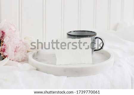 Wedding still life scene. Business, place card mockup scene, marble tray, cup of coffee an pink peony flowers on white linen table cloth. Vintage feminine styled photo. Floral festive composition.