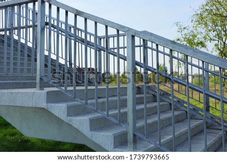 part of a gray pedestrian bridge made of concrete steps and iron handrails on the street