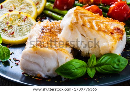 Fish dish - fried cod fillet with asparagus on wooden table  Royalty-Free Stock Photo #1739796365