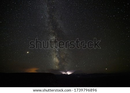 Starry sky with the Milky Way in the summer against the backdrop of the mountain with a flash of light