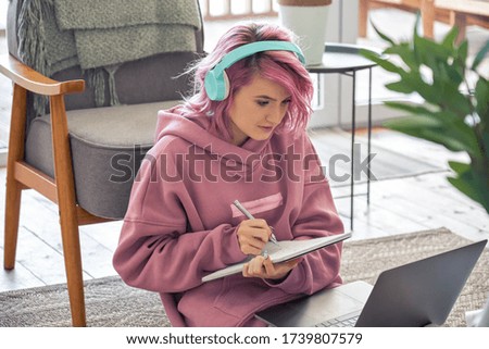 Focused hipster teen girl school college student pink hair wear headphones write notes watching webinar online video conference calling on laptop computer sit on floor working learning online at home. Royalty-Free Stock Photo #1739807579