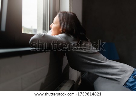 Woman sitting alone at home looking out window