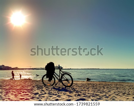 bike  and people  silhouettes  walking  on the beach sand at  summer sunset on sea on skyline ,reflection of sunlight on water  urban lifestyle 