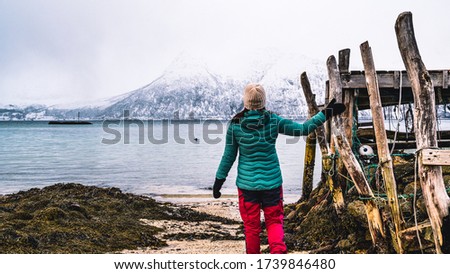 Girl holding on to an old wooden pier, looking over the fjord towards the snowy mountains