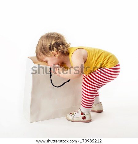 Cute little blonde girl reaching into a gift bag on a white background with surprised look on her face 