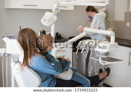 The boy on his mother's lap sitting on the dental chair, Due the Covid-19 pandemic they have face masks. Royalty-Free Stock Photo #1739855225