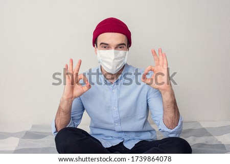 Smiling young man in the medical mask looks at the camera and show gesture ok, portrait, toned