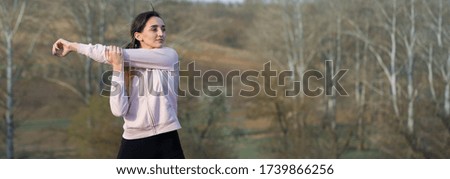 A young slim athletic girl in sportswear performs a set of exercises. Fitness and healthy lifestyle  against the background of green spring pasture hills.