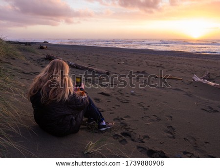 Woman siting on the sand taking a cell pic of the sunset with a loving chihuahua sleeping on her arm