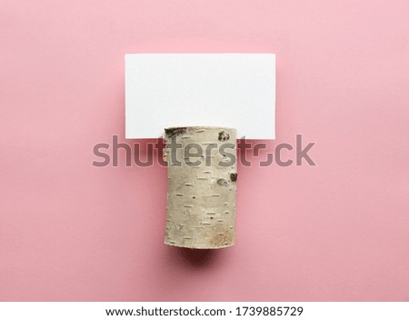 white empty card in birch wood holder on pink paper background, top view
