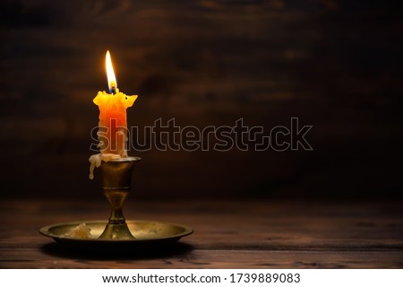 close up of burning old candle with vintage brass candlestick on wooden background in minimalist room interior 