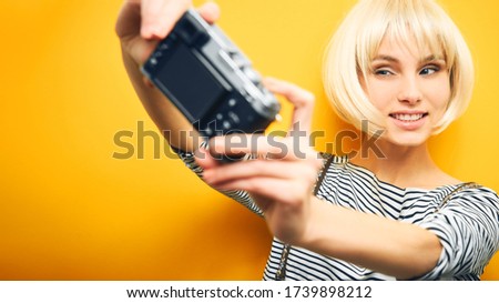 portrait of a girl in a striped sweater and a white wig makes a selfie on a camera on an orange background