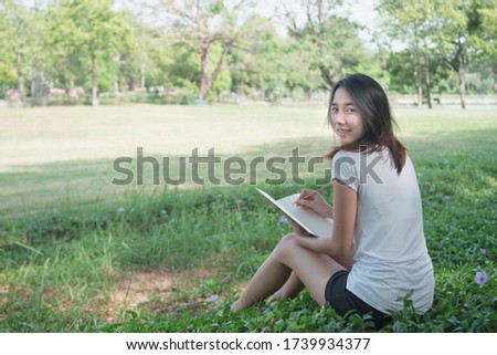 Digital detox concept. Asian beautiful woman reading a book by not use smartphone for relaxing activity without digital technology in the park on natural light freshness morning