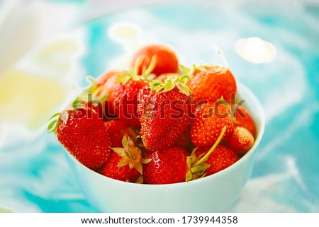 red juicy ripe strawberries in a blue vase on a light background on a blue stand made of epoxy resin. Healthy spring breakfast, fruit plate
