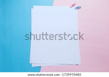 Two stacked white papers and clips on pastel color pink and blue background. Mock up. Minimalist. Blank space for text. 