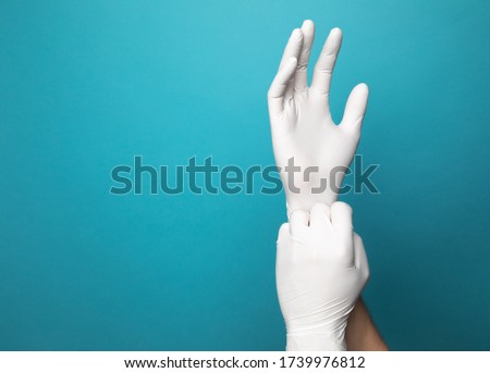 White latex gloves on two hands with a vibrant blue studio background. One gloved hand is pulling the end of the other glove down to simulate putting gloves on.  Royalty-Free Stock Photo #1739976812