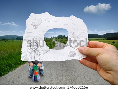 Young boy riding a small tricycle sketched on a hand held piece of paper with vanishing path and green countryside scenery in the photo background. Mixed media image.
