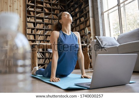 Happy fit sporty hispanic girl doing online yoga exercise stretch on mat at home. Active healthy latin woman enjoy sport pilates physical fitness training on laptop computer watching video class guide Royalty-Free Stock Photo #1740030257