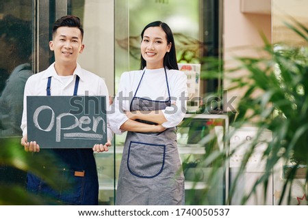Portrait of happy confident young waitress and waiter showing open sign and opening cafe