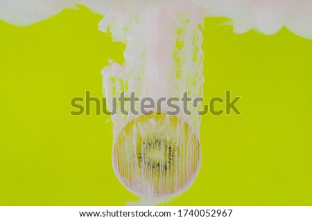 Blurred focus of dissolving pink poster color in water with slice kiwi fruit on yellow background for summer, abstract and background concept.