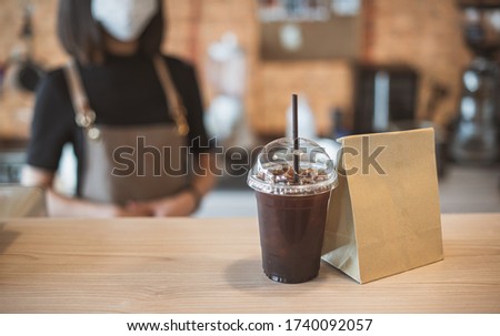 Barista  in apron and face mask standing  behind counter bar ready to give Coffee Service at the modern coffee shop, Modern cafe business, Social distancing concept.  Royalty-Free Stock Photo #1740092057