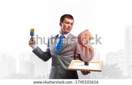 Creative businessman painter holding paint brush and dollar sign. Portrait of happy man in business suit and tie on modern cityscape background. Money exchange and capital investing.