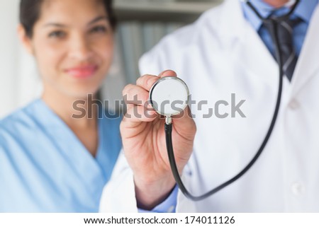 Midsection of male doctor holding stethoscope with nurse in background at hospital