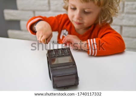 A little boy with long curly hair makes a card payment through the terminal.