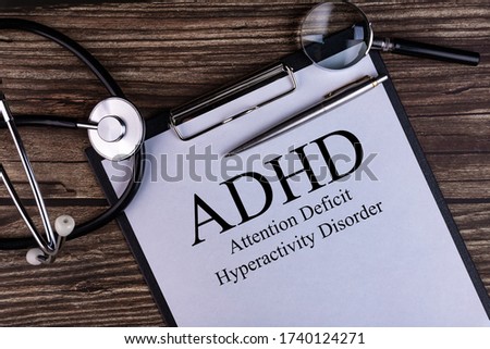 Notebook page with text ADHD - Attention Deficit Hyperactivity Disorder, on a table with a stethoscope and magnifier, medical concept.