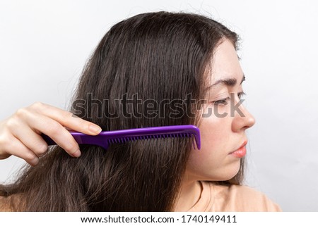 Dandruff and hair problems. A woman combs her long dark hair. Side view. White background