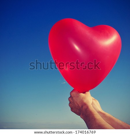 picture of someone holding a red heart-shaped balloon over the blue sky, with a retro effect