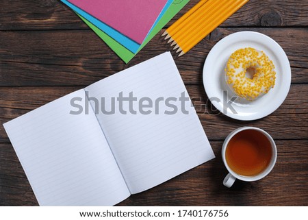 School notebooks, cup of tea and donut on dark wooden table, top view