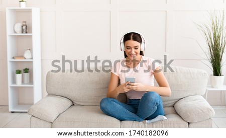 Student Girl With Smartphone Listening To Podcast In Earphones Learning Distantly Sitting On Sofa At Home. Weekend Leisure Concept. Panorama