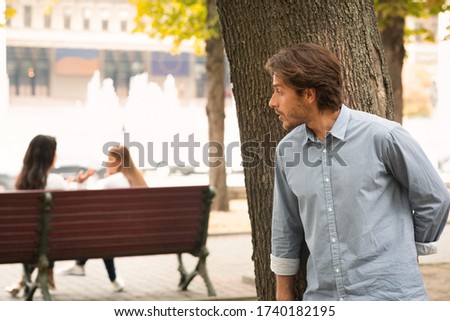 Suspicious Man Spying On Girls Stalking Them While They Talking Sitting In Park Royalty-Free Stock Photo #1740182195