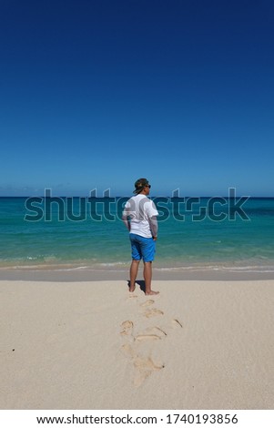 A male looking over the sea on a beautiful white sand and blue sky